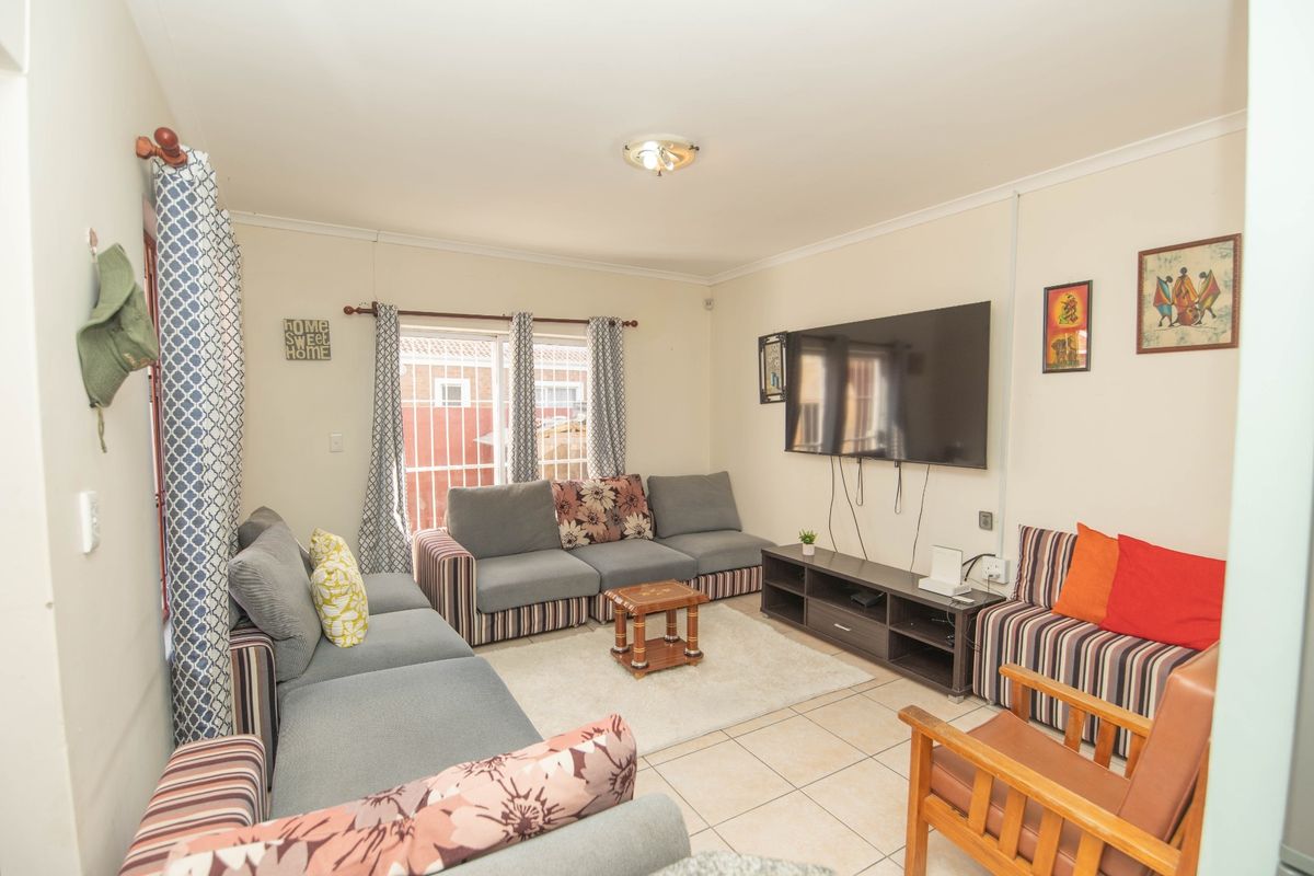 A functional living room featuring tiled flooring, a sliding door with security bars, and neutral wall finishes.