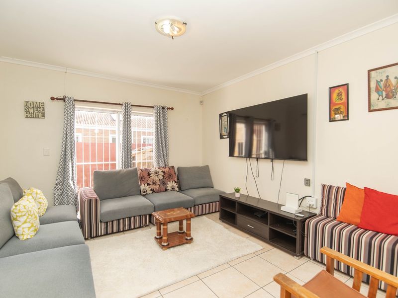 A comfortable living room featuring tiled flooring, a ceiling light fixture, and a sliding glass door with security bars providing natural light.
