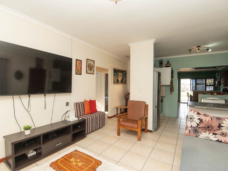 Open-plan living area featuring tiled flooring and coved cornicing, seamlessly connecting to a functional kitchen space with a breakfast counter.