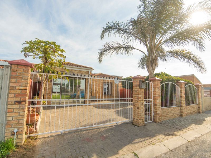 Front view of a brick-faced house featuring a paved driveway, secure metal gate, and perimeter brick walling.