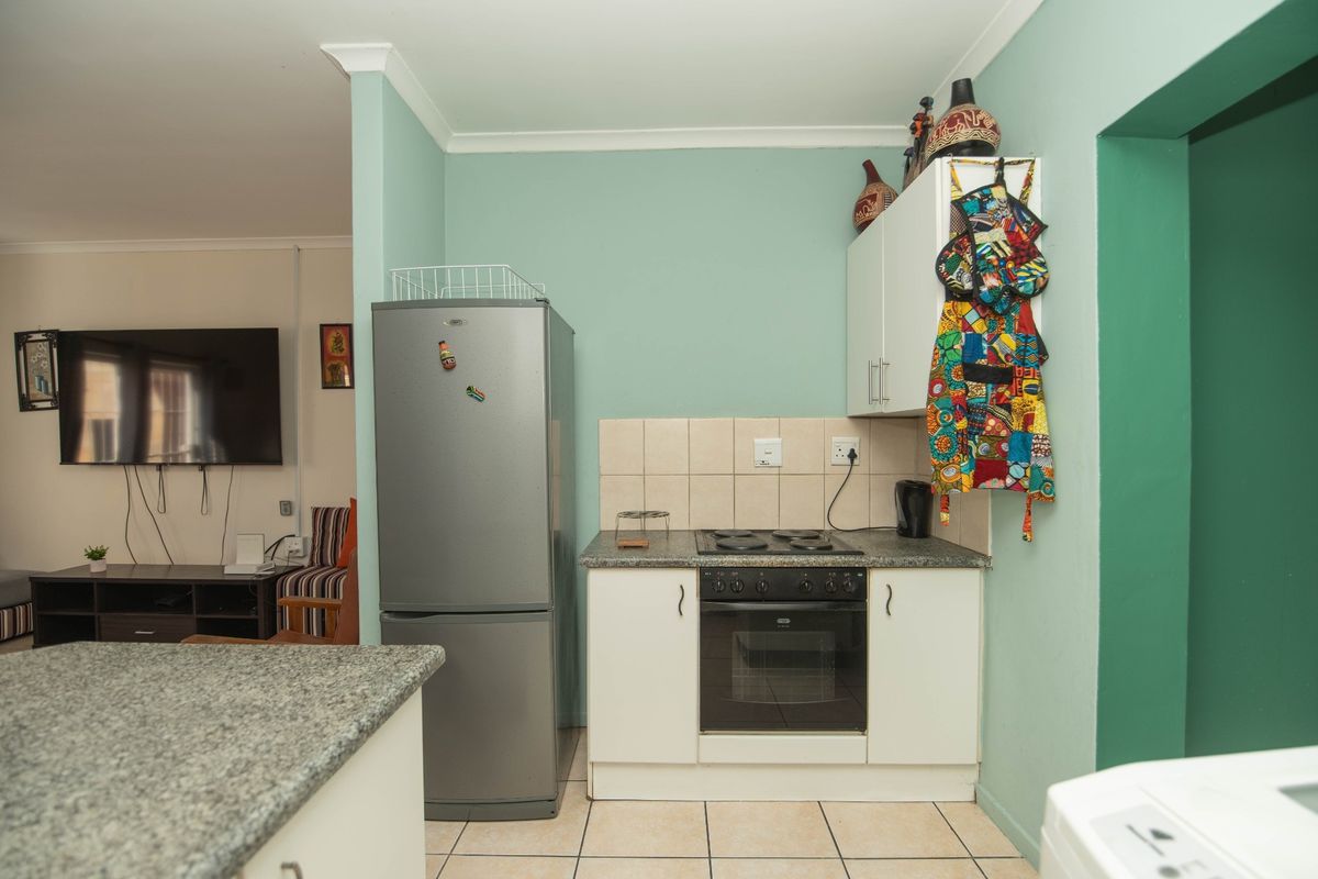 Compact kitchen area featuring built-in cabinetry, granite countertops, an integrated oven and hob, and a tiled backsplash, adjacent to the living space.
