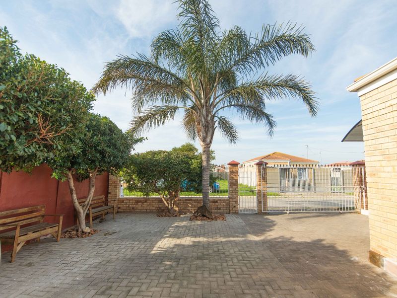 A paved front courtyard area featuring a brick boundary wall, metal security gate, and established palm tree.