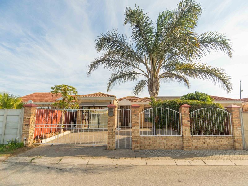 Front exterior view of a single-story house featuring a brick facade, tiled roof, paved driveway, and a secure gated entrance with boundary wall.