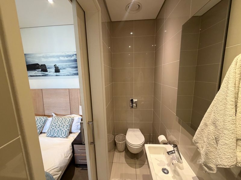 A compact, modern en-suite bathroom featuring neutral wall tiles, a wall-mounted toilet, and a sleek integrated basin with chrome fixtures.