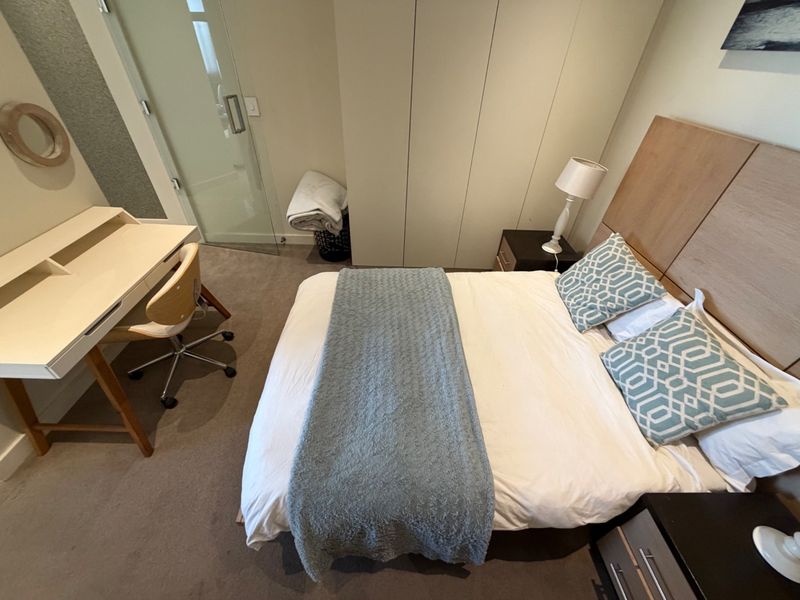 A well-maintained bedroom featuring built-in wardrobes, carpeted flooring, and an integrated glass door leading to an en-suite bathroom.