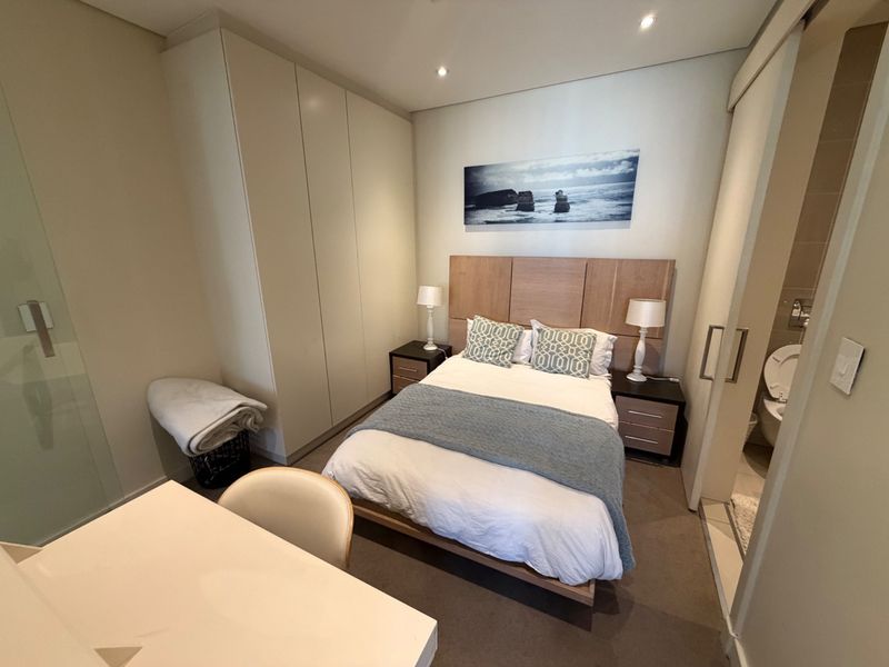 A modern bedroom featuring built-in cupboards, recessed lighting, and an en-suite bathroom with a sliding door entry.