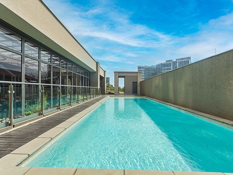 A modern, well-maintained lap pool featuring a glass balustrade, timber decking, and expansive glass facade overlooking the water.