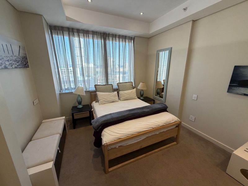 A well-maintained bedroom featuring neutral walls, carpet flooring, a recessed ceiling with downlights, and a large window providing natural light.