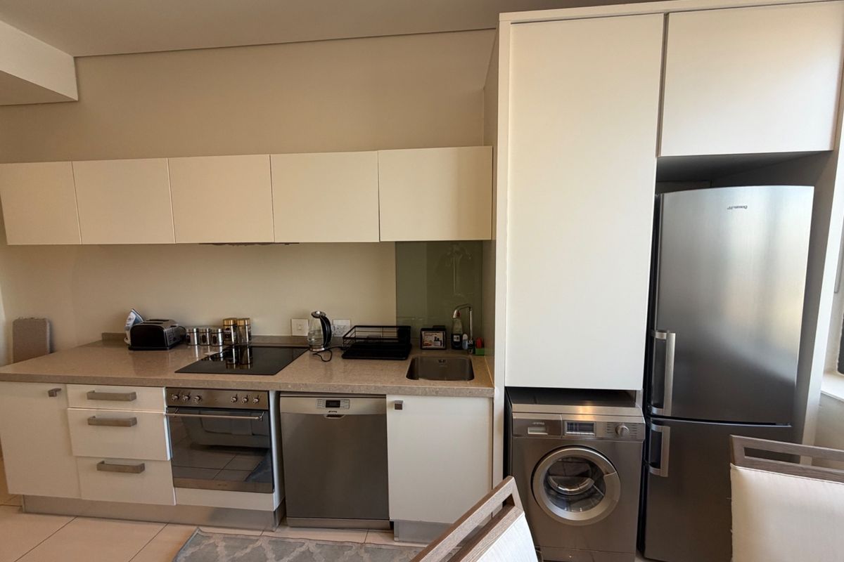 Modern kitchen featuring sleek white cabinetry, stone countertops, integrated stainless steel appliances including a dishwasher and washing machine, and a built-in electric hob and oven.