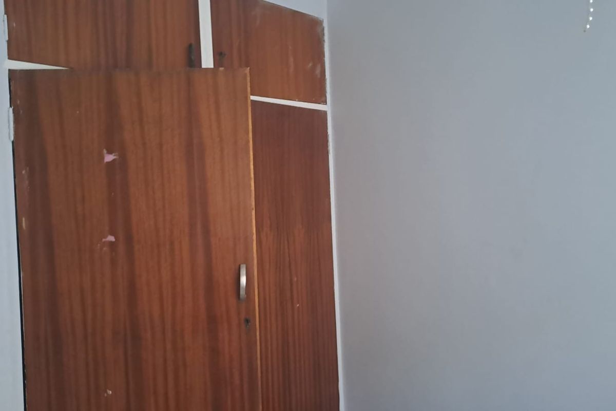 A vacant bedroom featuring dated built-in wooden cupboards and plain wall finishes, offering a blank canvas for potential renovation or modernization.