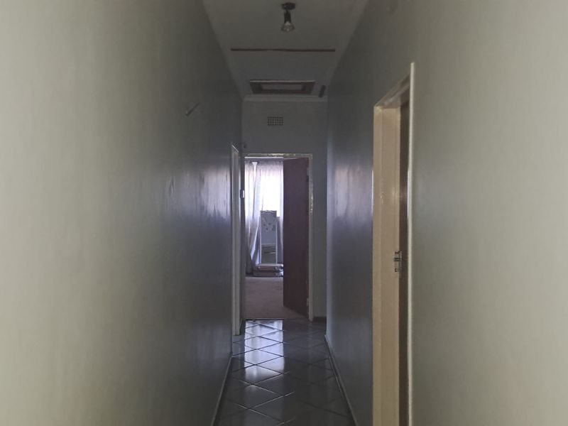 A narrow residential hallway featuring tiled flooring and a ceiling access hatch, leading towards an adjacent room.