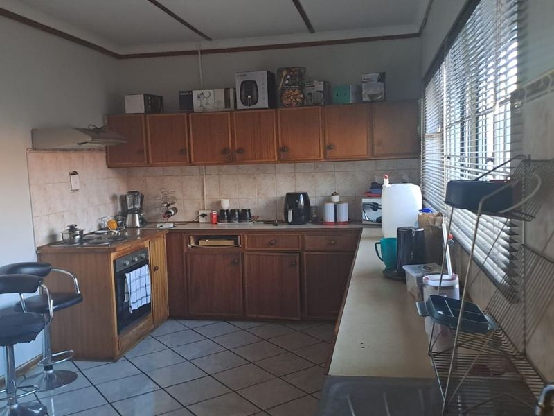 A functional kitchen featuring wooden cabinetry, built-in oven, hob, extractor fan, and tiled flooring, offering potential for a modern renovation.