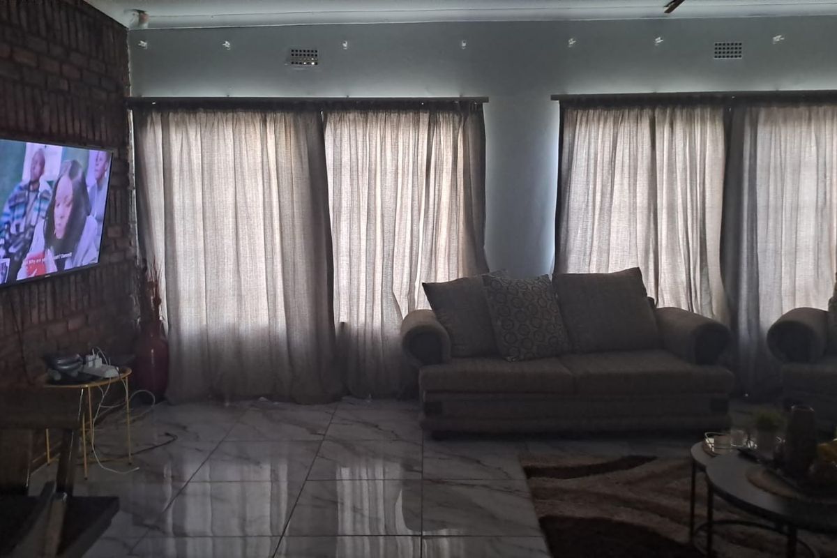 A living room featuring an exposed brick feature wall, polished tiled flooring, and large windows with curtains.