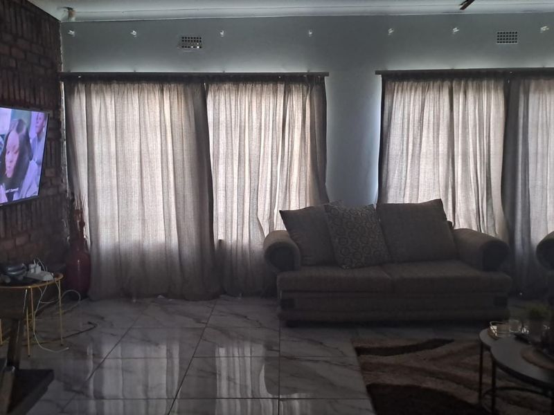 A living room featuring an exposed brick feature wall, polished tiled flooring, and large windows with curtains.