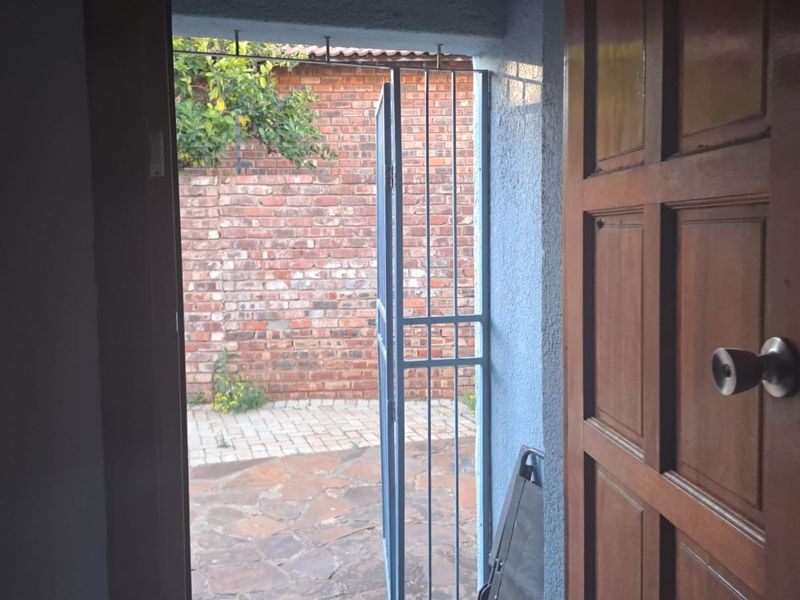 An interior view looking through an open timber door and security gate towards a paved outdoor patio and brick boundary wall.