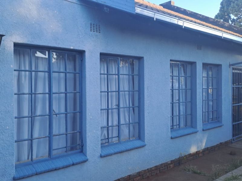 Front elevation of a residential house featuring blue plastered walls, steel-framed windows with security bars, and a tiled roof.
