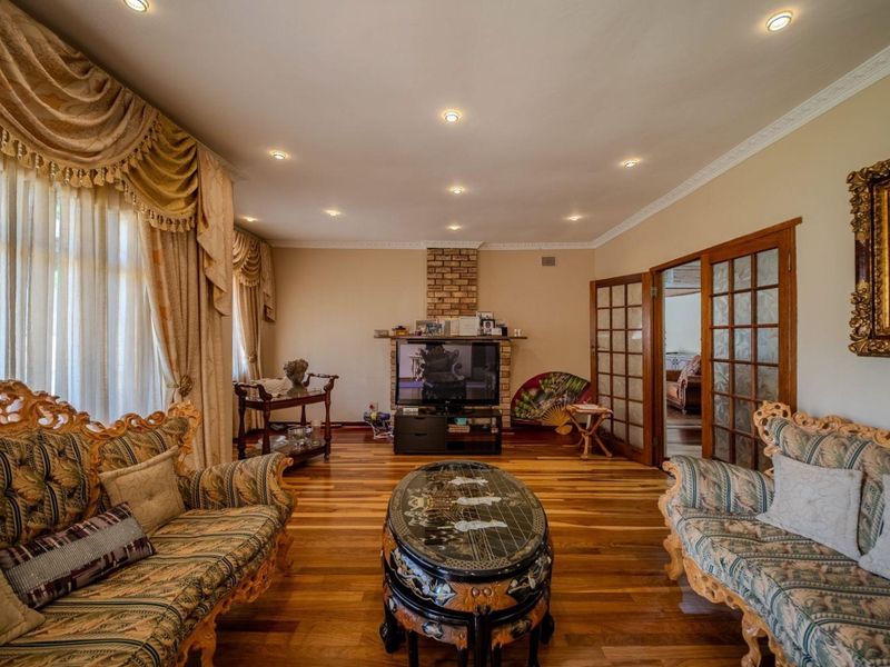 Spacious living room featuring polished hardwood flooring, a brick fireplace, and elegant French doors leading to adjacent living areas.
