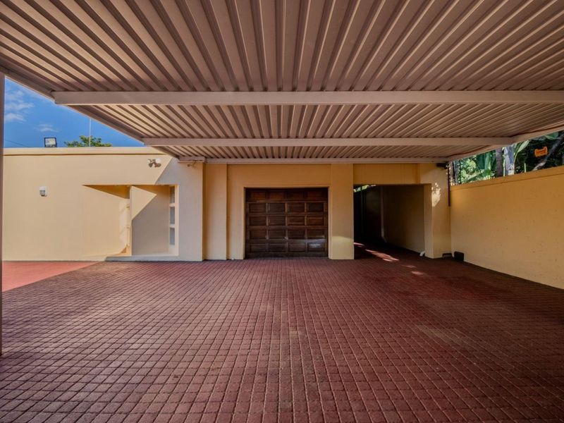 A spacious covered carport area featuring a paved driveway and a secure sectional garage door, providing ample off-street parking.
