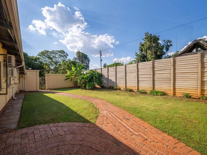 A private rear garden featuring a well-maintained lawn, a curved brick paved pathway, and secure precast concrete boundary walls.