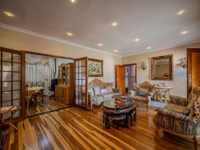 Spacious living room featuring polished hardwood flooring, recessed downlighting, crown molding, and elegant french doors leading to an adjacent dining area.