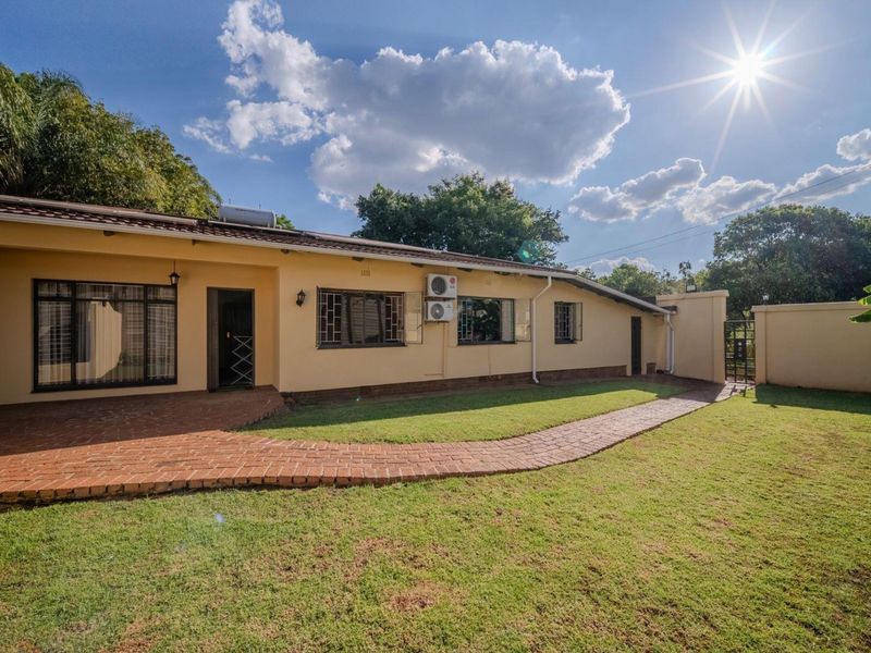 Rear view of the property featuring a brick paved patio, landscaped lawn, perimeter wall, and exterior mounted air conditioning units.