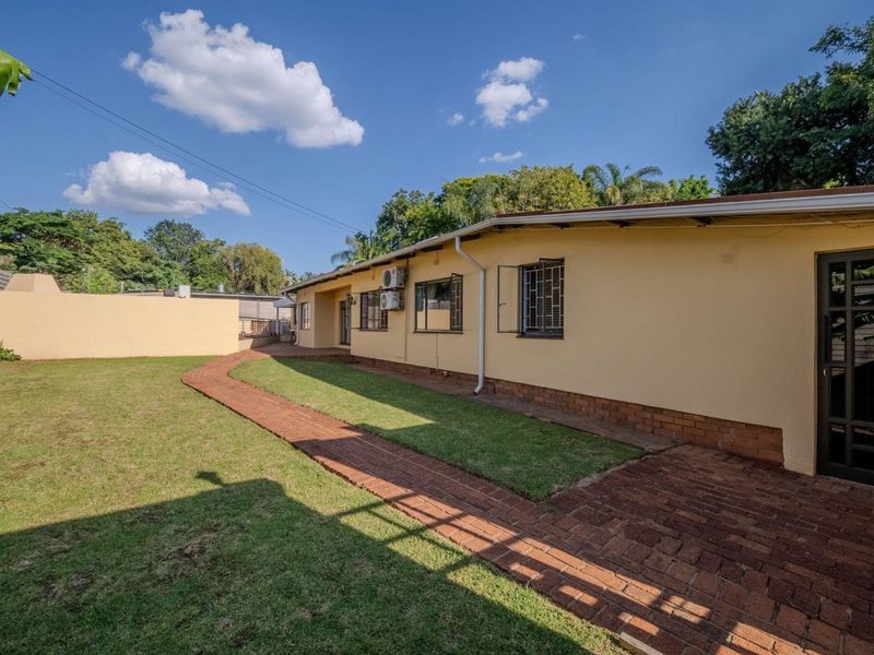 Rear view of the property featuring a paved walkway, well-maintained lawn, and secure exterior wall finishes.