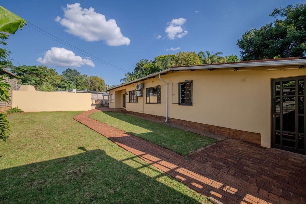 Rear view of the property featuring a paved walkway, well-maintained lawn, and secure exterior wall finishes.