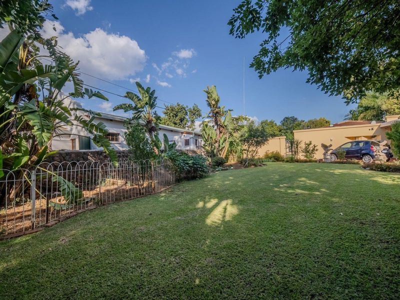 A well-maintained garden featuring a spacious lawn, mature trees, and a stone retaining wall with metal perimeter fencing.