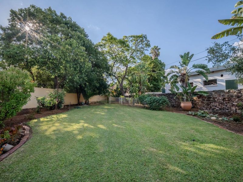 A well-maintained private garden featuring a spacious lawn, mature trees, and a rustic stone retaining wall.