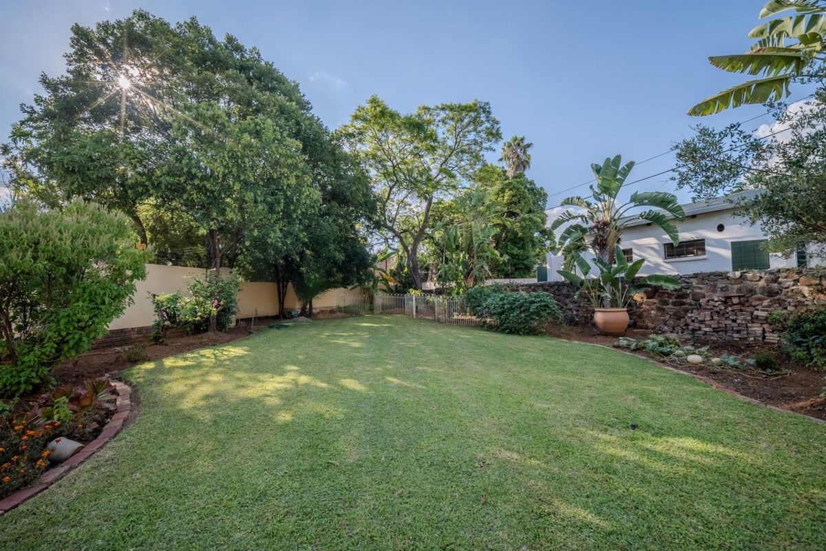 A well-maintained private garden featuring a spacious lawn, mature trees, and a rustic stone retaining wall.