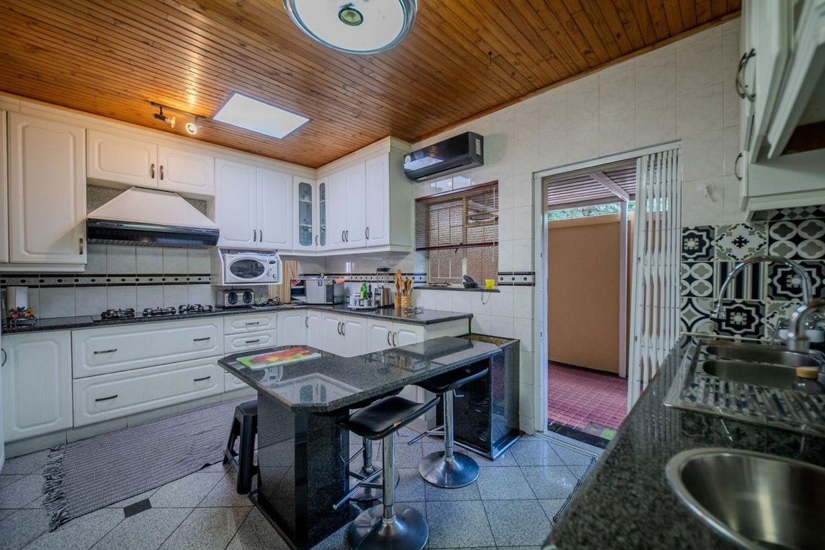 A functional kitchen featuring granite countertops, white cabinetry, a gas hob, and a timber-paneled ceiling, with direct access to an outdoor area.