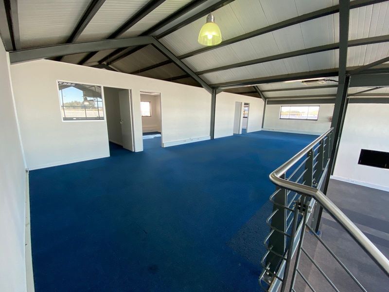 Spacious open-plan office area featuring exposed steel roof trusses, blue carpeting, and a modern stainless steel balustrade overlooking the lower level.