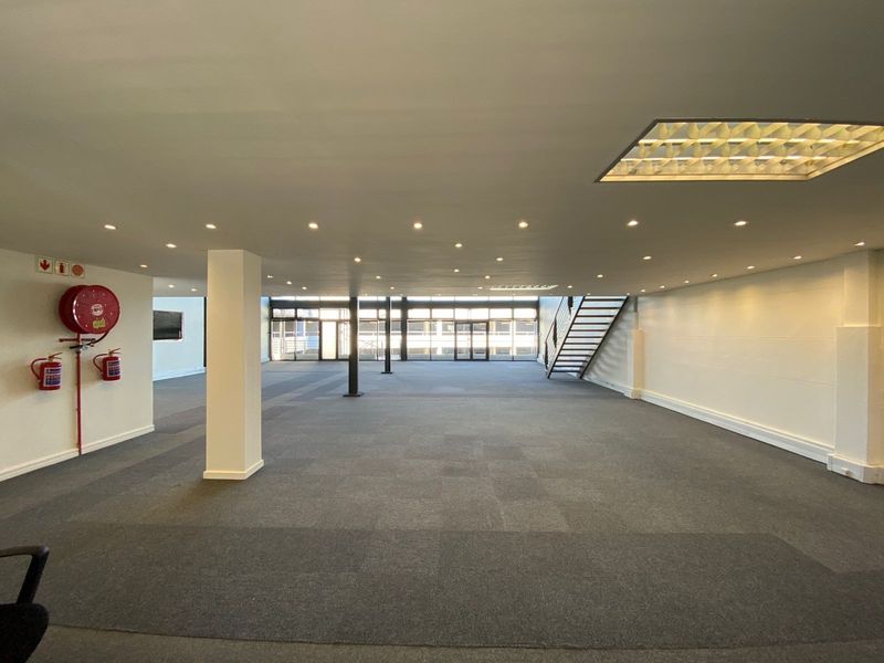 Spacious open-plan office area featuring recessed lighting, carpeted flooring, structural columns, and a staircase, offering a clean and versatile workspace.