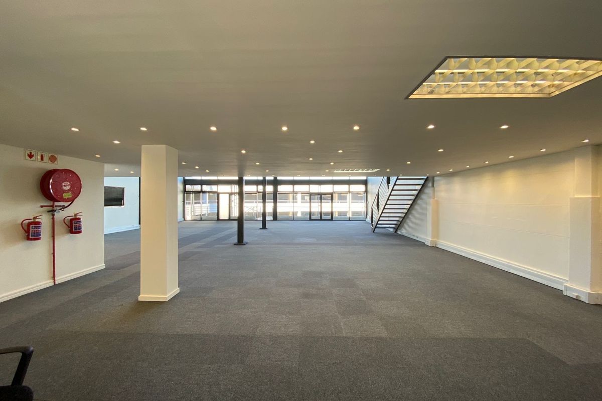 Spacious open-plan office area featuring recessed lighting, carpeted flooring, structural columns, and a staircase, offering a clean and versatile workspace.