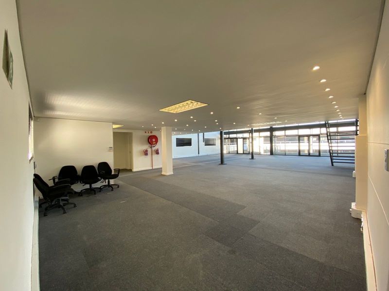 Spacious open-plan office area featuring neutral carpeting, recessed lighting, and large windows providing ample natural light, suitable for a flexible workspace layout.