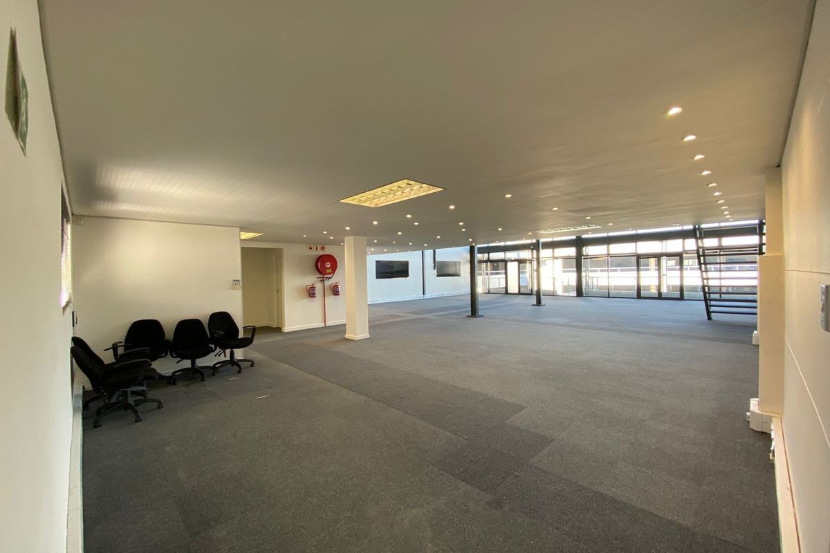 Spacious open-plan office area featuring neutral carpeting, recessed lighting, and large windows providing ample natural light, suitable for a flexible workspace layout.