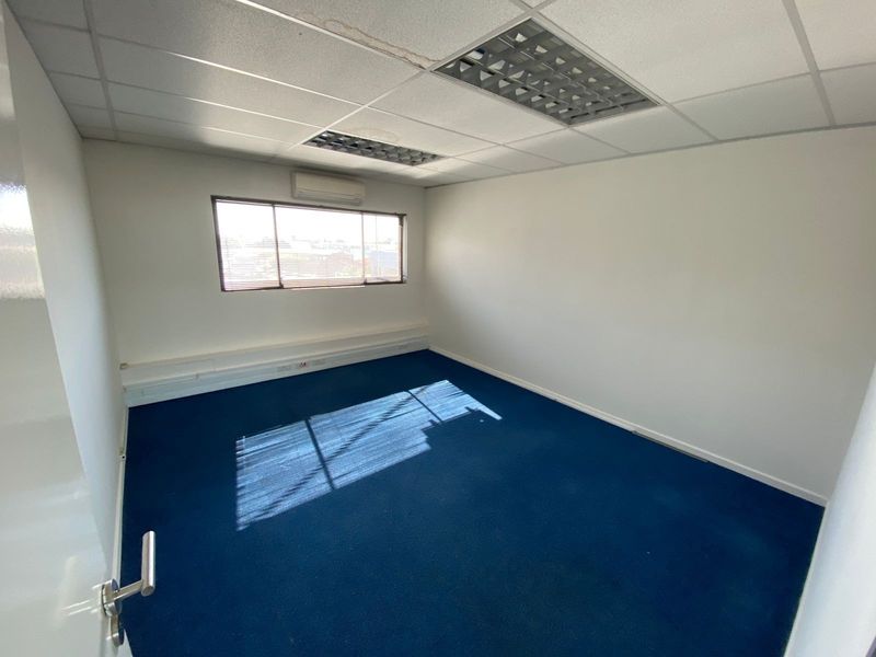 A vacant office space featuring blue carpeting, a suspended ceiling with recessed lighting, and a wall-mounted air conditioning unit.