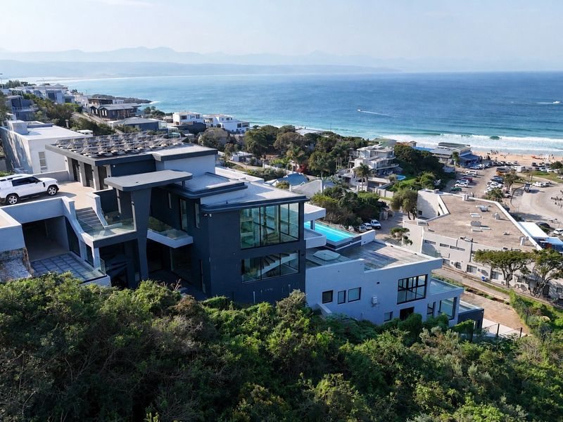 Aerial view of a modern multi-level coastal residence featuring solar panels, a swimming pool, and expansive glass windows overlooking the ocean.