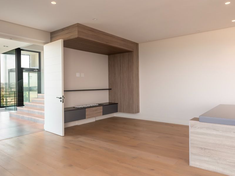 Modern living area featuring high-quality timber flooring, custom built-in media cabinetry with slat detailing, and recessed lighting, leading to an adjacent staircase.