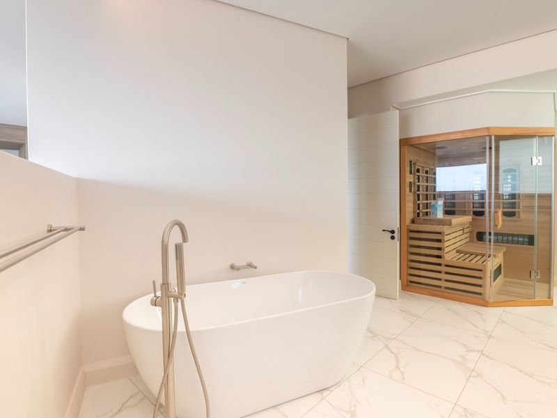Modern bathroom featuring a sleek freestanding bathtub, floor-mounted mixer, and a built-in sauna with glass enclosure and marble-look tiled flooring.