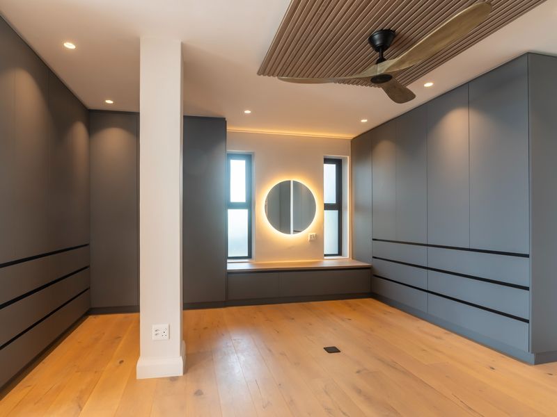 Modern bedroom featuring extensive built-in cabinetry, timber flooring, a decorative timber ceiling panel with a fan, and a backlit vanity mirror.