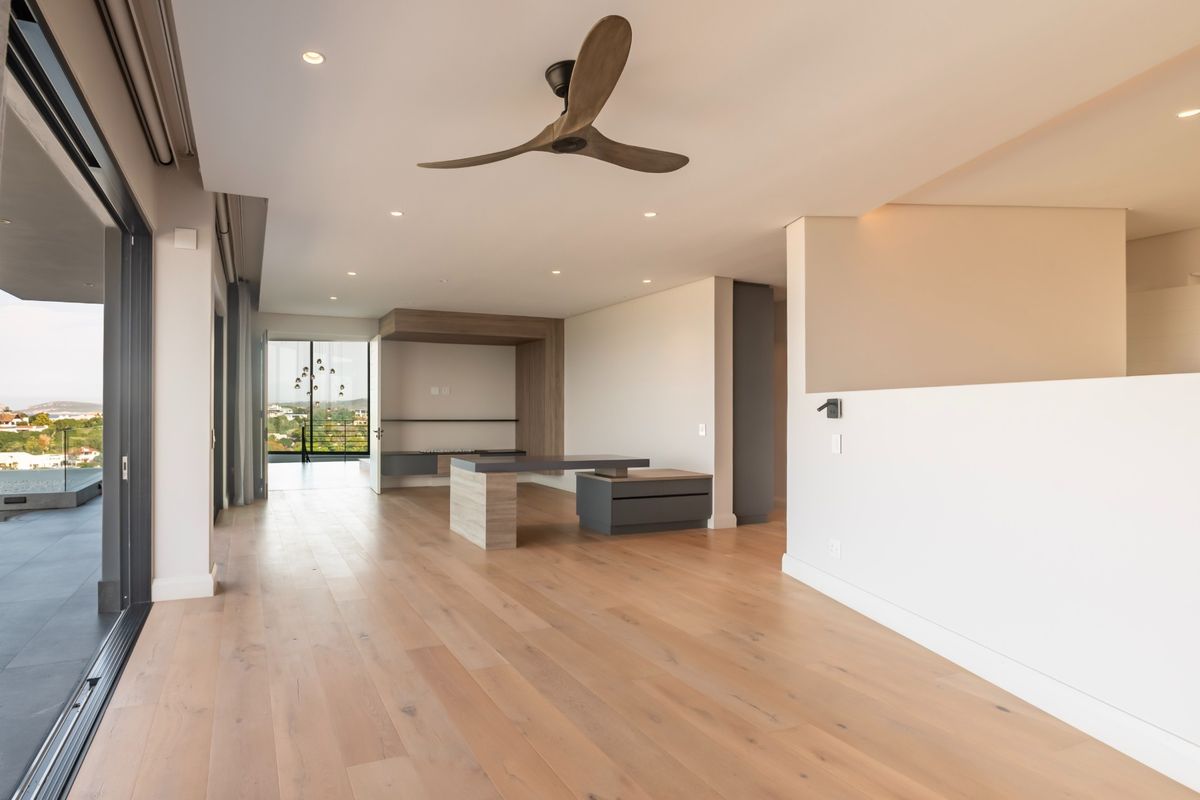 Spacious, modern living area featuring light hardwood flooring, recessed lighting, a designer ceiling fan, and large sliding doors opening to a balcony with views.
