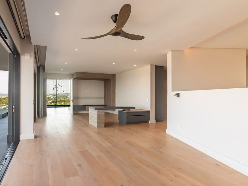 Spacious, modern living area featuring light hardwood flooring, recessed lighting, a designer ceiling fan, and large sliding doors opening to a balcony with views.