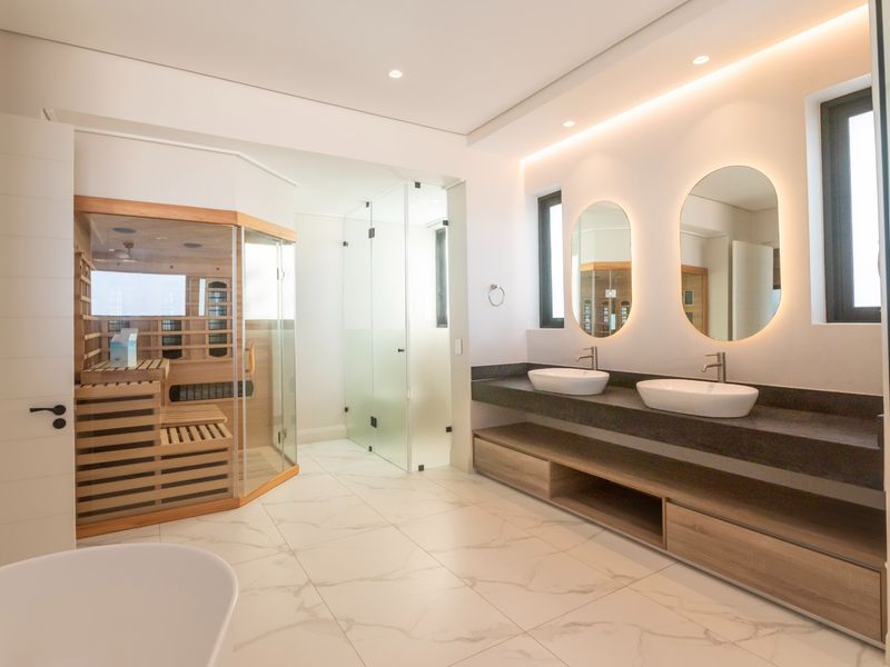 Modern luxury bathroom featuring a double vanity with vessel sinks, backlit mirrors, a glass-enclosed shower, and a built-in sauna.