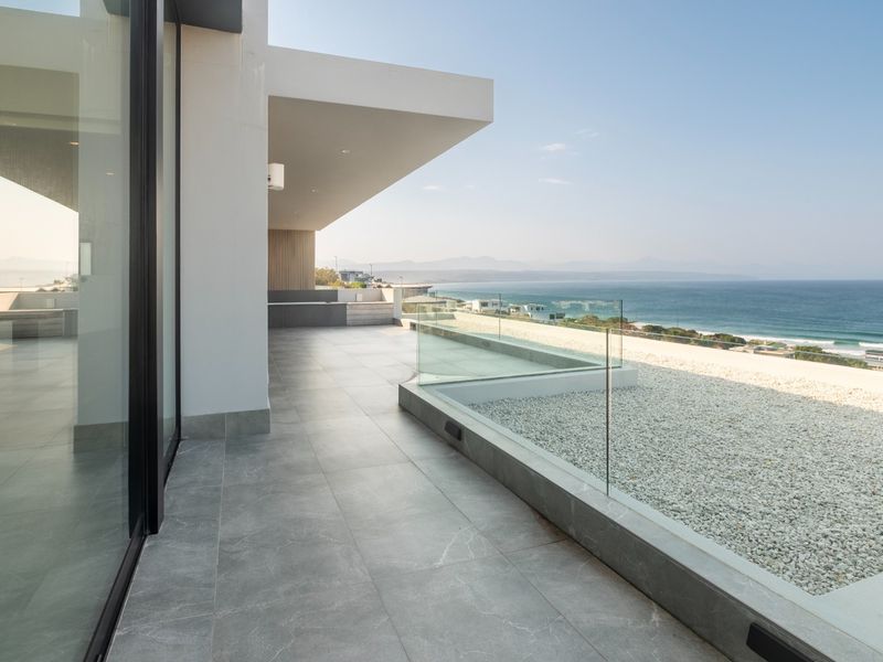 A modern, spacious balcony featuring sleek tiled flooring, a frameless glass balustrade, and expansive ocean views.