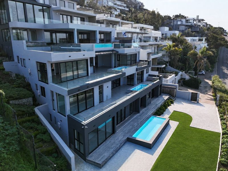 Aerial view of a modern multi-level luxury residence featuring multiple swimming pools, expansive glass-fronted terraces, and landscaped outdoor areas.