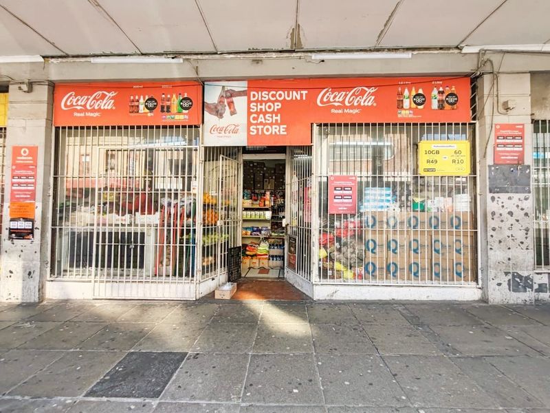 Street-level retail shopfront featuring a security gate, prominent signage, and a paved entrance area.