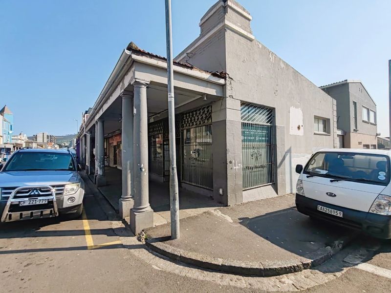 Street-level view of a retail property featuring a covered walkway with classical columns, security-barred display windows, and a weathered concrete facade.