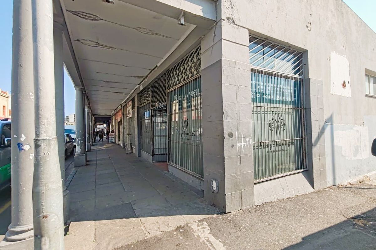 Street-level view of a retail storefront featuring a covered walkway, security grilles, and large display windows in need of exterior maintenance.