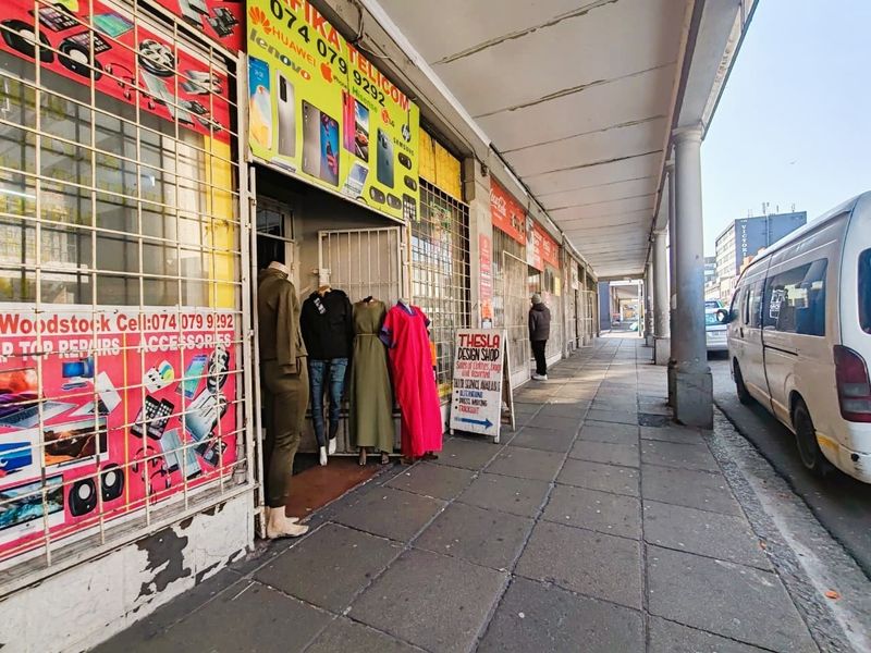 Street-level view of a retail storefront featuring a covered walkway, security gates, and signage along a paved sidewalk.